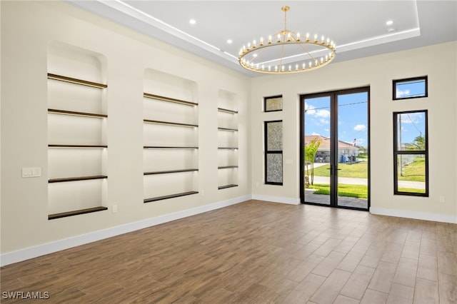 3413 NW 9th Ter, Cape Coral, FL 33993 - spare room featuring built in features, a tray ceiling, baseboards, a chandelier, and wood finished floors