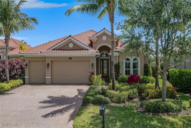 mediterranean / spanish-style home with stucco siding, an attached garage, decorative driveway, and a tiled roof