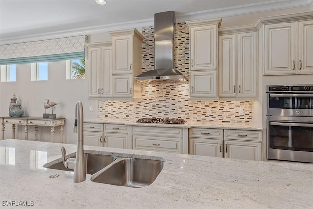 kitchen featuring wall chimney exhaust hood, cream cabinetry, a sink, stainless steel appliances, and crown molding