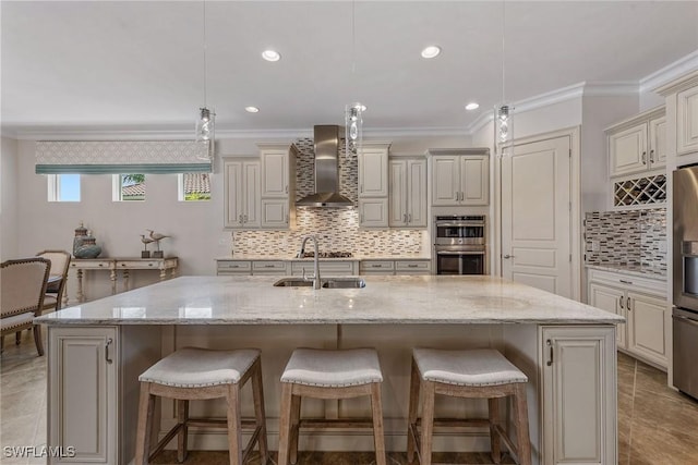 kitchen with wall chimney exhaust hood, a sink, decorative backsplash, crown molding, and cream cabinetry