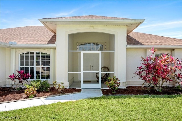 property entrance featuring a shingled roof, a yard, and stucco siding