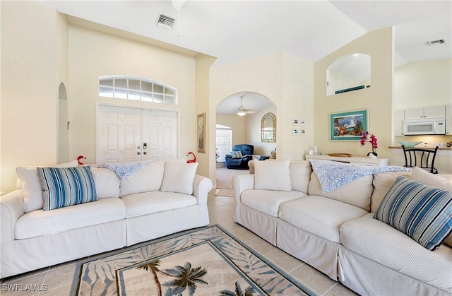 tiled living area featuring arched walkways and high vaulted ceiling