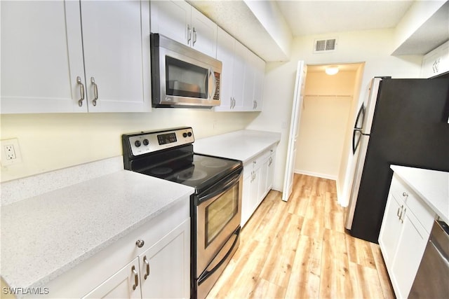 kitchen with stainless steel appliances, white cabinetry, light wood-style flooring, and light stone countertops