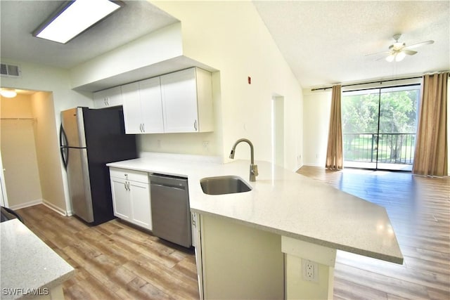 kitchen with appliances with stainless steel finishes, a sink, a peninsula, light wood-style flooring, and white cabinetry