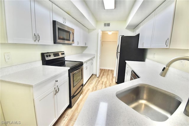 kitchen with stainless steel appliances, a sink, white cabinets, light stone countertops, and light wood-style floors
