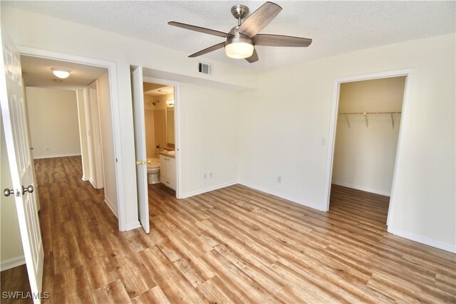 unfurnished bedroom with a closet, light wood finished floors, a spacious closet, baseboards, and ceiling fan