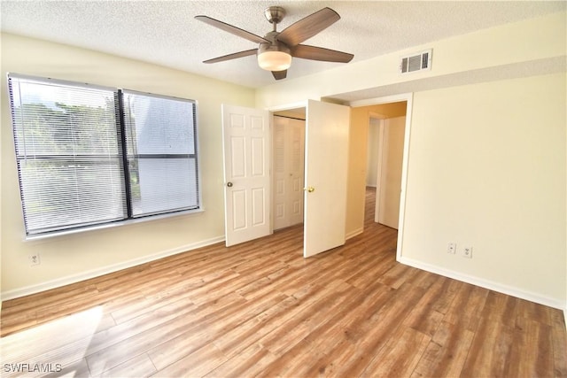unfurnished bedroom featuring light wood-style flooring, a textured ceiling, baseboards, a ceiling fan, and a closet