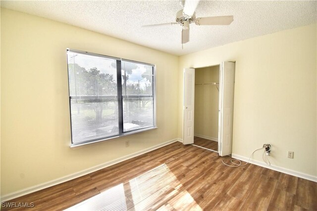 unfurnished bedroom featuring wood finished floors, a textured ceiling, a closet, baseboards, and a ceiling fan