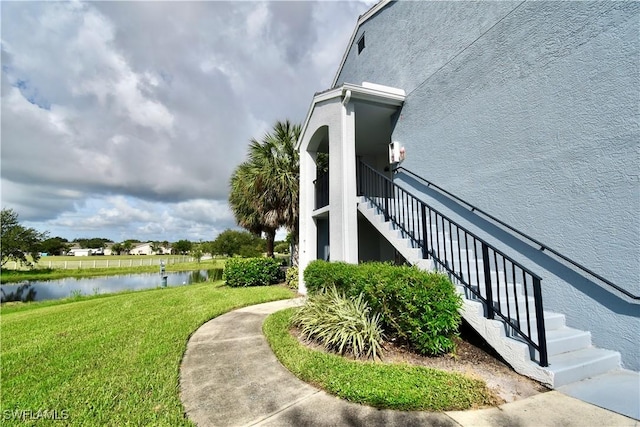 view of side of home with stairway, a water view, a lawn, and stucco siding