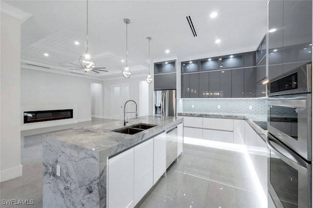 333 12th Ave NE, Naples, FL 34120 - kitchen with modern cabinets, a sink, a glass covered fireplace, stainless steel appliances, and decorative backsplash