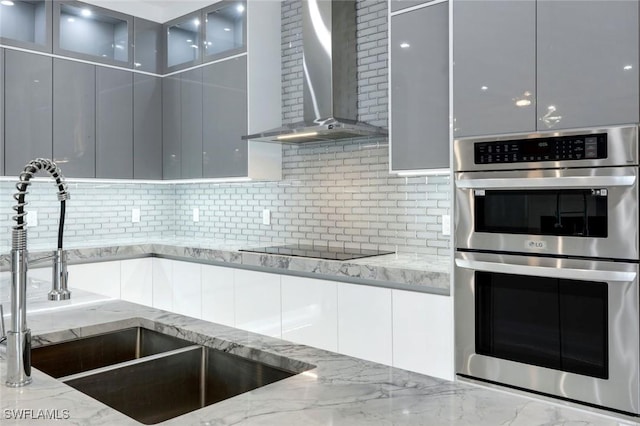 333 12th Ave NE, Naples, FL 34120 - kitchen featuring wall chimney exhaust hood, a sink, double oven, modern cabinets, and decorative backsplash