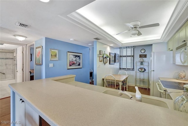 kitchen featuring white appliances, a tray ceiling, a ceiling fan, light countertops, and a sink