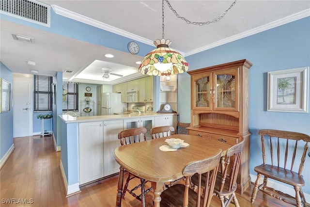dining area featuring baseboards, ornamental molding, wood-type flooring, ceiling fan, and a tray ceiling