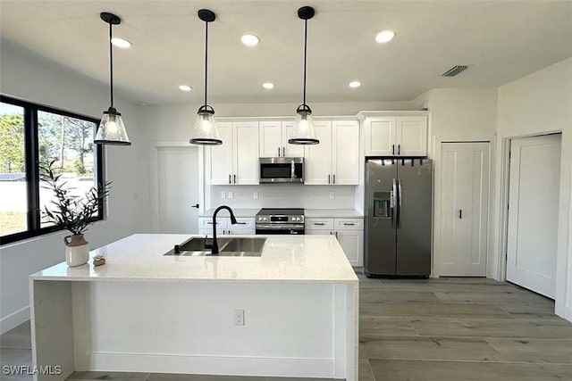 kitchen featuring stainless steel appliances, a sink, white cabinetry, recessed lighting, and a kitchen island with sink