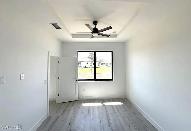 unfurnished room with a tray ceiling, baseboards, wood finished floors, and a ceiling fan