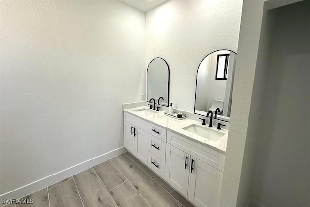 full bath featuring double vanity, wood finished floors, baseboards, and toilet