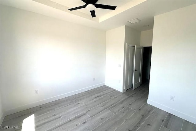 unfurnished room with ceiling fan, wood finished floors, baseboards, and a raised ceiling