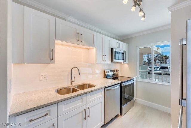 kitchen featuring appliances with stainless steel finishes, a sink, decorative backsplash, white cabinetry, and ornamental molding