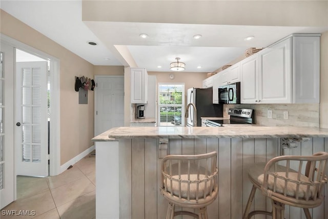 676 W Elkcam Cir Unit 1222, Marco Island, FL 34145 - kitchen featuring appliances with stainless steel finishes, light stone counters, a peninsula, decorative backsplash, and light tile patterned flooring