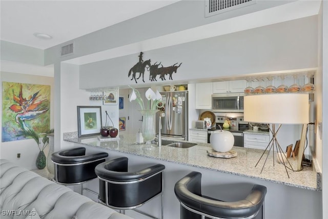 6573 Marissa Loop Unit 303, Naples, FL 34108 - kitchen featuring stainless steel appliances, a peninsula, white cabinets, light stone counters, and a kitchen breakfast bar