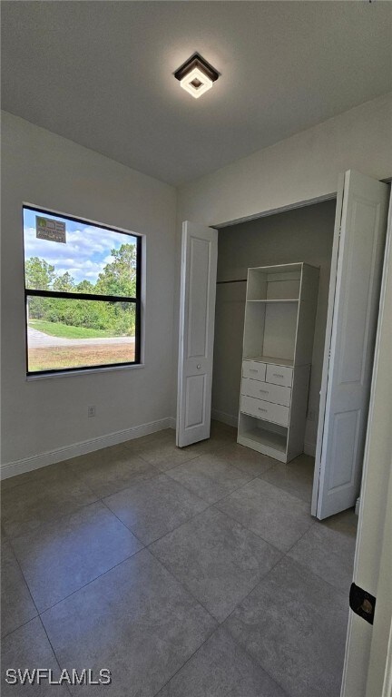 1019 Calvin Ave, Lehigh Acres, FL 33972 - unfurnished bedroom with tile patterned flooring, baseboards, and a closet
