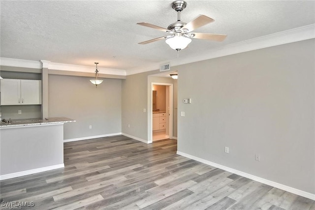 unfurnished living room with ceiling fan, wood finished floors, a textured ceiling, baseboards, and ornamental molding