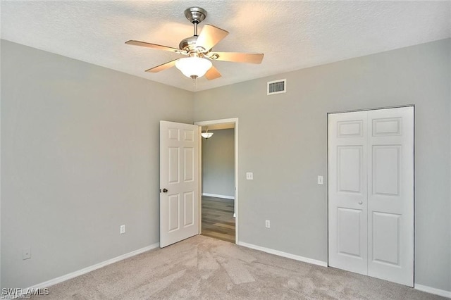 unfurnished bedroom with light carpet, baseboards, a textured ceiling, ceiling fan, and a closet