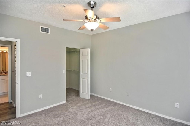 unfurnished bedroom featuring a spacious closet, carpet flooring, a closet, baseboards, and a ceiling fan