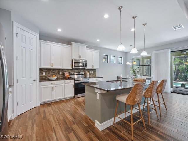 kitchen with stainless steel appliances, dark wood finished floors, tasteful backsplash, a sink, and white cabinetry