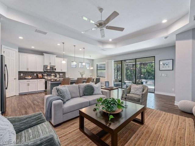 living room featuring a tray ceiling, wood finished floors, ceiling fan, recessed lighting, and baseboards