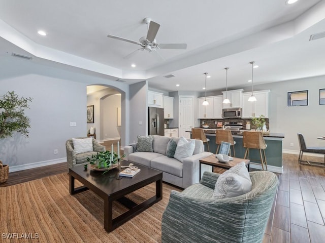 living area with arched walkways, ceiling fan, wood finished floors, baseboards, and recessed lighting
