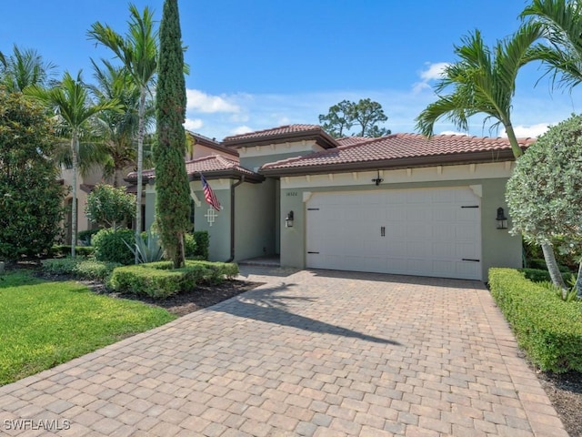 mediterranean / spanish house featuring stucco siding, a garage, decorative driveway, a tile roof, and a front yard
