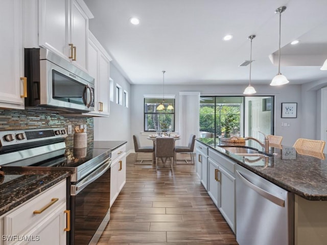 kitchen with appliances with stainless steel finishes, a sink, dark wood-style flooring, tasteful backsplash, and white cabinets