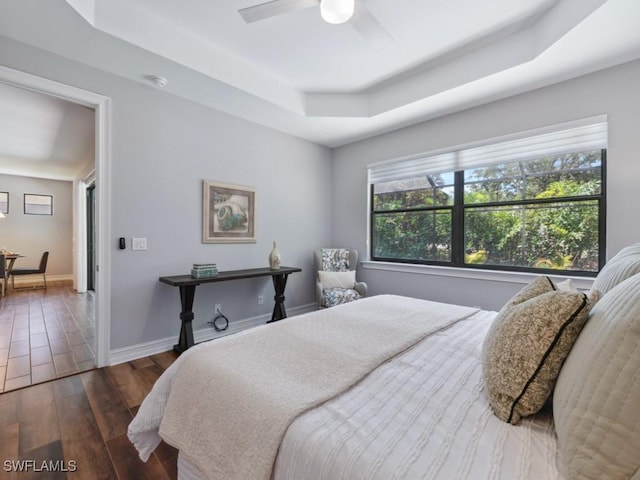 bedroom featuring a raised ceiling, dark wood finished floors, baseboards, and a ceiling fan