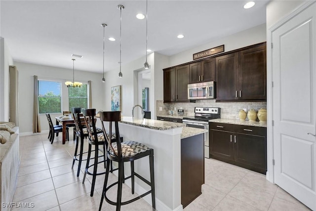 kitchen featuring appliances with stainless steel finishes, a breakfast bar, decorative backsplash, light stone countertops, and a chandelier