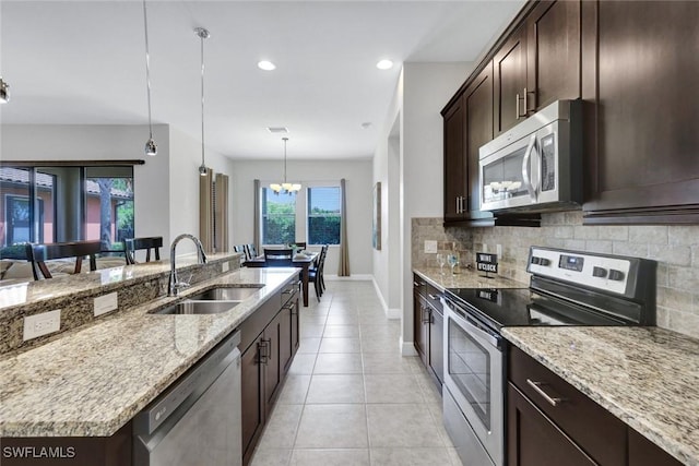 kitchen with appliances with stainless steel finishes, a sink, tasteful backsplash, dark brown cabinets, and light stone countertops