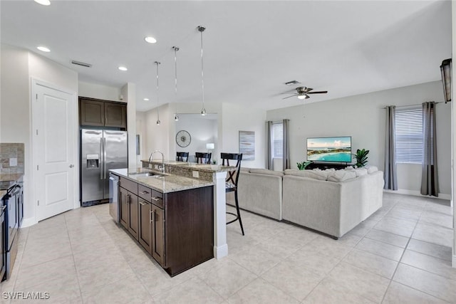 kitchen with a sink, appliances with stainless steel finishes, a kitchen breakfast bar, a ceiling fan, and dark brown cabinets
