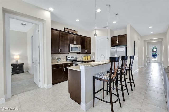 kitchen with appliances with stainless steel finishes, dark brown cabinetry, a kitchen bar, decorative backsplash, and light tile patterned floors