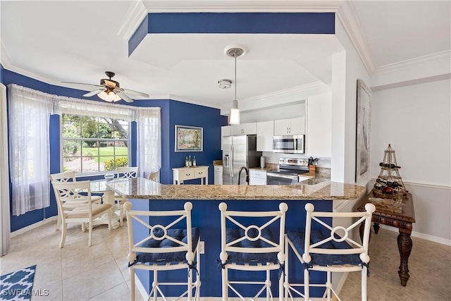 kitchen featuring appliances with stainless steel finishes, white cabinets, light stone countertops, a ceiling fan, and baseboards