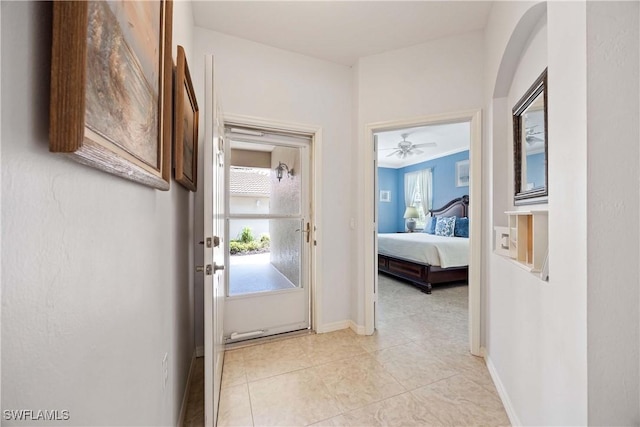 hall with arched walkways, baseboards, and light tile patterned floors