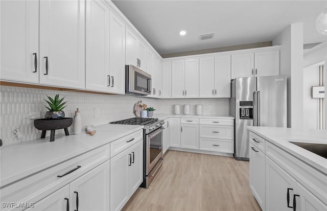 12429 Basalt Ln, Alva, FL 33982 - kitchen featuring stainless steel appliances, white cabinets, light countertops, light wood-style flooring, and backsplash