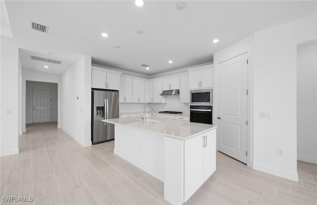 12429 Basalt Ln, Alva, FL 33982 - kitchen featuring appliances with stainless steel finishes, under cabinet range hood, light countertops, white cabinets, and a kitchen island with sink