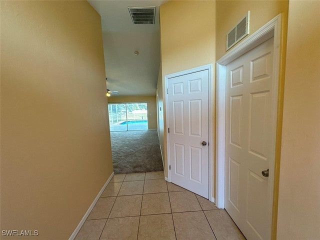 corridor featuring baseboards, light tile patterned floors, and light colored carpet
