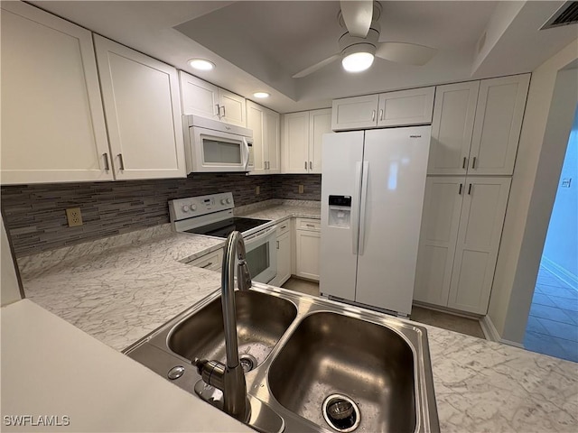 kitchen with white appliances, a sink, backsplash, light countertops, and white cabinets