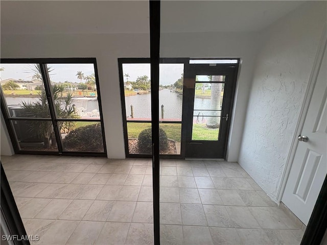 doorway to outside with a water view, a textured wall, and light tile patterned flooring