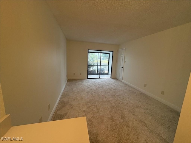 empty room featuring light carpet, a textured ceiling, and baseboards