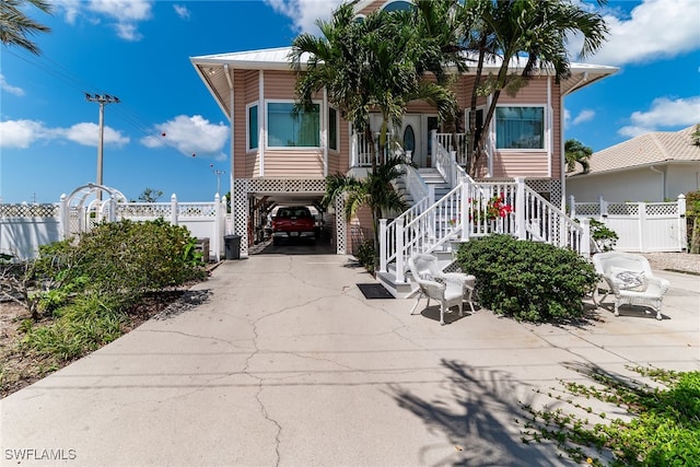 view of front of home featuring a carport, stairs, fence, concrete driveway, and covered porch