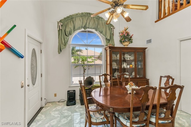 dining room featuring a ceiling fan, a high ceiling, and light marble finish flooring