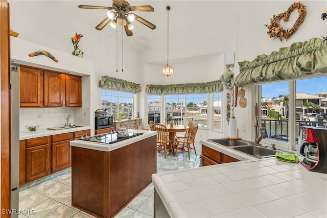kitchen featuring tile countertops, black electric cooktop, high vaulted ceiling, a sink, and a ceiling fan