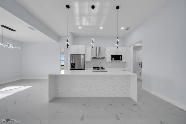kitchen with stainless steel appliances, a sink, wall chimney exhaust hood, white cabinetry, and a kitchen island with sink
